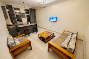 Cozy living room and kitchenette in Ebenezer Hotel Apartments Nyarugunga unit, with sofa, TV, bar stools, ideal for stays near Kigali's top neighborhoods.
